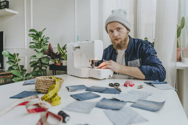 Fashion designer wearing knit hat sitting with sewing machine in workshop - YTF00346