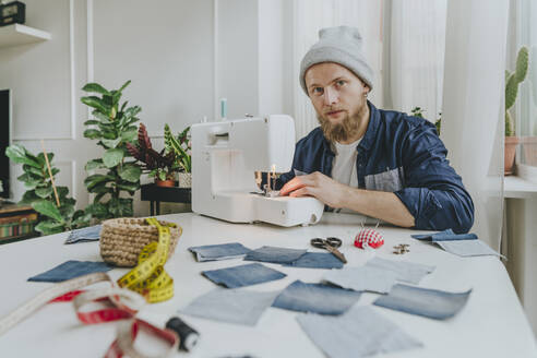 Modedesignerin mit Strickmütze, sitzend mit Nähmaschine in der Werkstatt - YTF00346