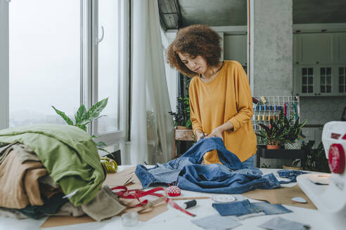 Junge Modedesignerin schneidet Jeans mit einer Schere in einem Workshop zu - YTF00365