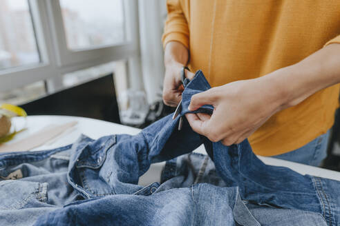 Hände eines jungen Modedesigners, der in einer Werkstatt Jeans mit einer Schere zuschneidet - YTF00366