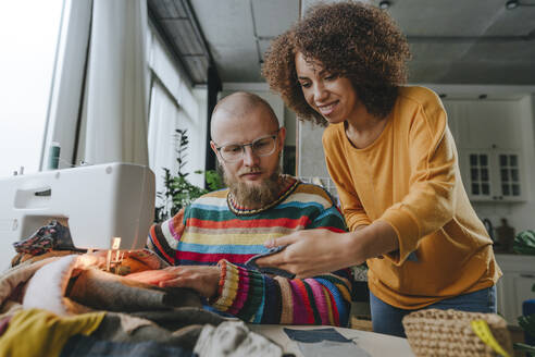 Smiling fashion designer showing denim fabric to colleague in workshop - YTF00370