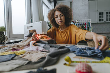 Young fashion designer sitting with clothes and sewing machine at table - YTF00372