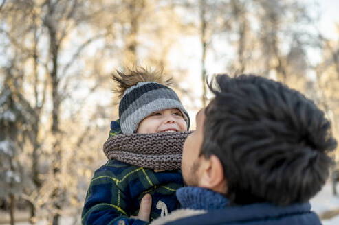 Mann trägt glücklichen Sohn mit Strickmütze im Winter - ANAF00656