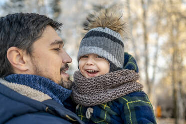 Vater trägt glücklichen Sohn mit Strickmütze im Winter - ANAF00659