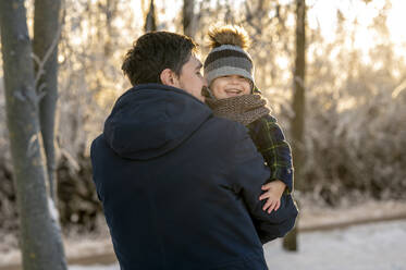 Smiling man carrying happy son in winter park - ANAF00663