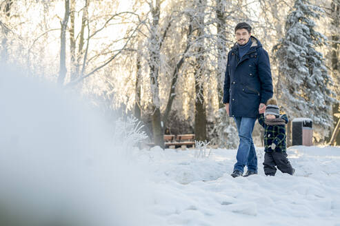 Mann hält die Hand seines Sohnes beim Spaziergang im Winterpark - ANAF00674