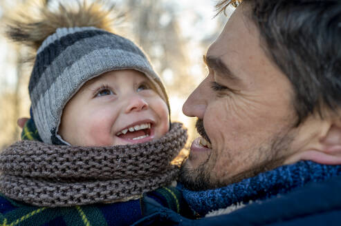 Happy man with son wearing warm clothing in winter - ANAF00678