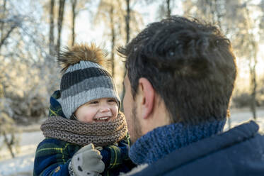 Glücklicher süßer Junge mit Vater in warmer Kleidung im Winterpark - ANAF00679