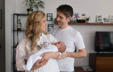 Eine lächelnde Mutter und ein Vater, die ihre neugeborene Tochter zu Hause im Arm halten - HPIF04331
