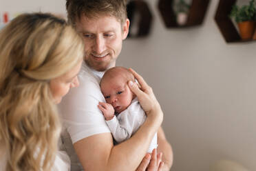 Eine glückliche Mutter und ein glücklicher Vater halten ihre neugeborene Tochter zu Hause im Arm - HPIF04334