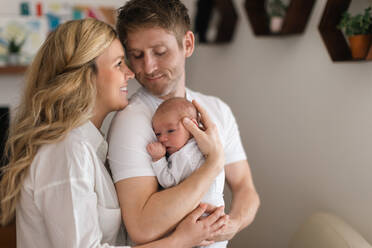Eine lächelnde Mutter und ein Vater, die ihre neugeborene Tochter zu Hause im Arm halten - HPIF04335