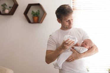 Ein Vater hält seinen neugeborenen Sohn im Arm und füttert ihn zu Hause mit der Milchflasche. - HPIF04346