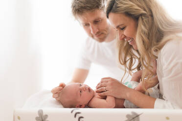 Happy parents bonding with their newborn son who is lying on a changing mat at home. - HPIF04347