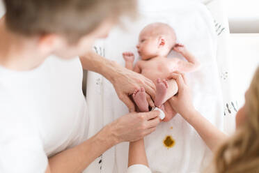 Eltern wickeln gemeinsam ihren neugeborenen Sohn, der zu Hause auf einer Wickelunterlage liegt, in eine Windel. - HPIF04349