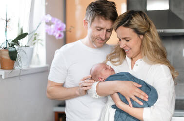 A smiling mother and father holding their newborn baby daughter at home - HPIF04353