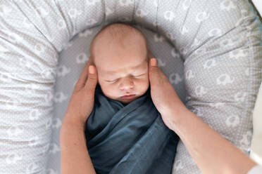 A newborn baby boy sleeping and swaddled in blue cloth lying in grey nest. - HPIF04355