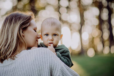 A mother holding her little baby son wearing knitted sweater during walk in nature, close-up - HPIF04360