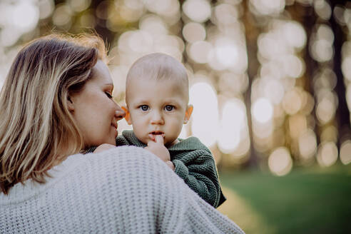 Eine Mutter hält ihren kleinen Sohn, der einen gestrickten Pullover trägt, während eines Spaziergangs in der Natur, Nahaufnahme - HPIF04360