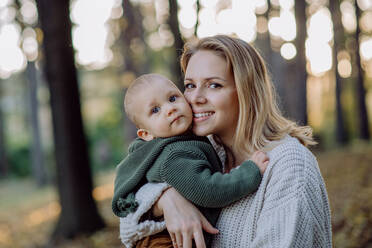 A mother holding her little baby son wearing knitted sweater during walk in nature, looking at camera. - HPIF04365