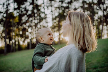 A mother holding her little baby son wearing knitted sweater during walk in nature, close-up - HPIF04372