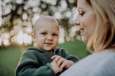 A mother holding her little baby son wearing knitted sweater during walk in nature, close-up - HPIF04373