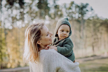Eine Mutter hält ihren kleinen Sohn im Arm und trägt einen gestrickten Pullover während eines Spaziergangs in der Natur. - HPIF04383