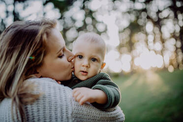 A mother holding her little baby son wearing knitted sweater during walk in nature. - HPIF04390
