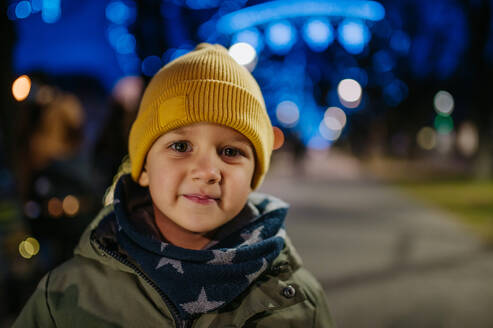 Porträt eines kleinen Jungen in Winterkleidung auf einem Weihnachtsmarkt in der Stadt. - HPIF04403