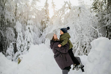 Mutter hält ihren großen Sohn in der winterlichen Natur und genießt den Schnee. - HPIF04404