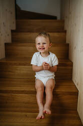 Ein süßes kleines Mädchen, das zu Hause auf der Treppe sitzt und in die Kamera schaut. - HPIF04422