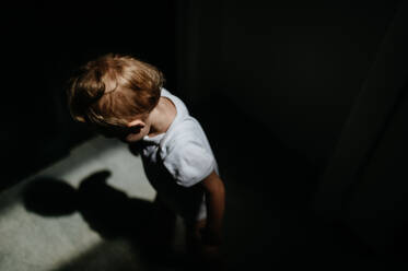 A dark high angle view portrait of sad anonymous little baby girl looking down. - HPIF04424