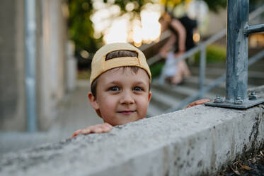 A little cute boy with looking over wall outdoors in summer - HPIF04441