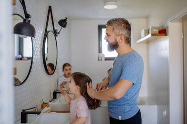 Ein Vater, der seiner kleinen Tochter im Badezimmer die Haare bürstet, Konzept der Morgenroutine. - HPIF04442