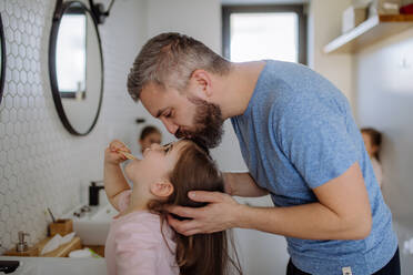 Ein Vater, der seine Tochter küsst, während sie sich im Badezimmer die Zähne putzt, Konzept der Morgenroutine. - HPIF04443