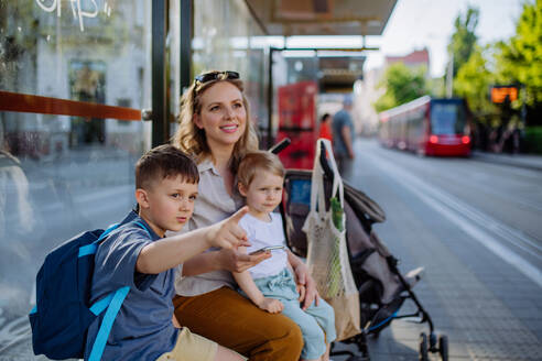 Eine junge Mutter mit kleinen Kindern wartet an einer Bushaltestelle in der Stadt. - HPIF04453
