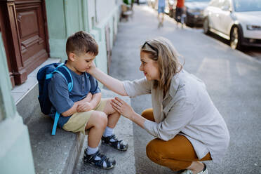Eine Mutter, die ihren kleinen Sohn an seinem ersten Schultag tröstet, auf der Treppe sitzt und sich vor der Schule verabschiedet. - HPIF04462