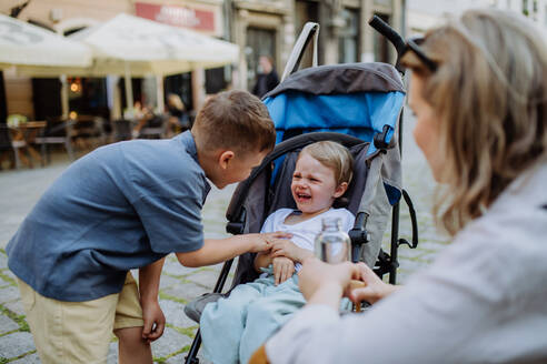 Eine Mutter und ihr kleiner Bruder beruhigen ein weinendes Mädchen, das in einem Kinderwagen sitzt, während sie die Straße entlanggehen - HPIF04466