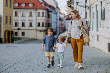 A young mother with zero waste shopping bag holding hands with her children and walking in city street street - HPIF04469