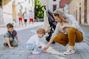 A little children with mother drwing with chalks on sidewalk in city on summer sunny day. Creative development of children. - HPIF04472