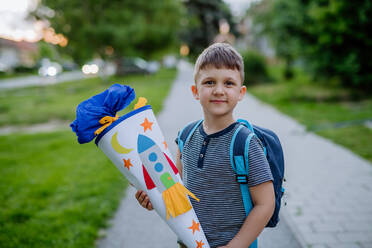 Ein kleiner Junge mit Schulranzen am ersten Schultag, der eine Schultüte mit Geschenken hält - HPIF04487