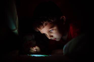 Ein süchtiger kleiner Junge spielt nachts im Bett Spiele auf seinem Handy. - HPIF04488