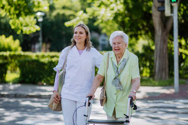 A caregiver with senior woman on walk with walker in park with shopping bag. - HPIF04517