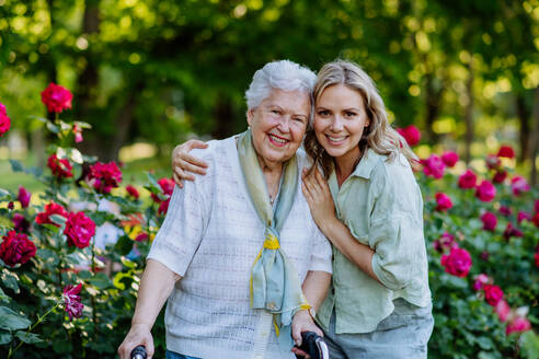 Ein Porträt von erwachsenen Enkelin mit älteren Großmutter auf Spaziergang im Park, mit Rosen im Hintergrund - HPIF04532