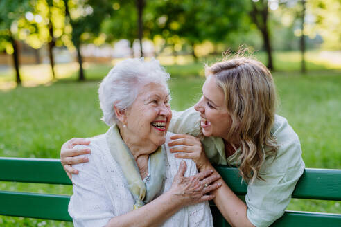 An adult granddaguhter helping her grandmother to use cellphone when sitting on bench in park in summer. - HPIF04539