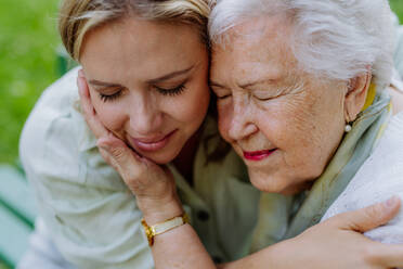 Nahaufnahme einer erwachsenen Enkelin und einer älteren Großmutter, die sich kuscheln, einen zärtlichen Moment genießen, sich umarmen, ihre Liebe ausdrücken und auf einer Bank im Park sitzen. - HPIF04545