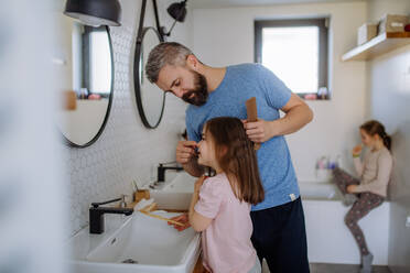 Ein Vater, der seiner kleinen Tochter im Badezimmer die Haare bürstet, Konzept der Morgenroutine. - HPIF04547