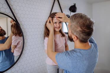 Ein Vater, der seiner kleinen Tochter im Badezimmer die Haare bürstet, Konzept der Morgenroutine. - HPIF04549