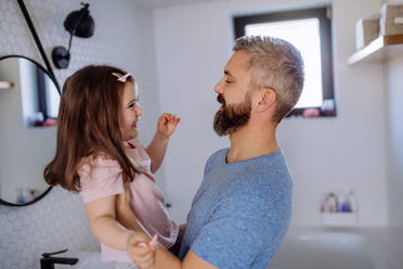 Ein glücklicher Vater mit seiner kleinen Tochter im Badezimmer, Morgenroutine Konzept. - HPIF04551