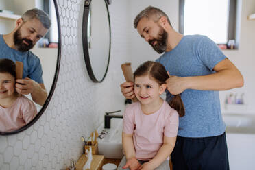 Ein Vater, der seiner kleinen Tochter im Badezimmer die Haare bürstet, Konzept der Morgenroutine. - HPIF04560