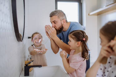 Ein Vater hat Spaß daran, mit seinen kleinen Töchtern im Badezimmer Seifenblasen zu machen. - HPIF04562